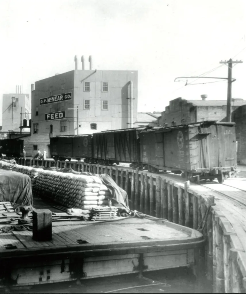 A historic train on the Petaluma trestle beside a barge loaded with feed sacks.
