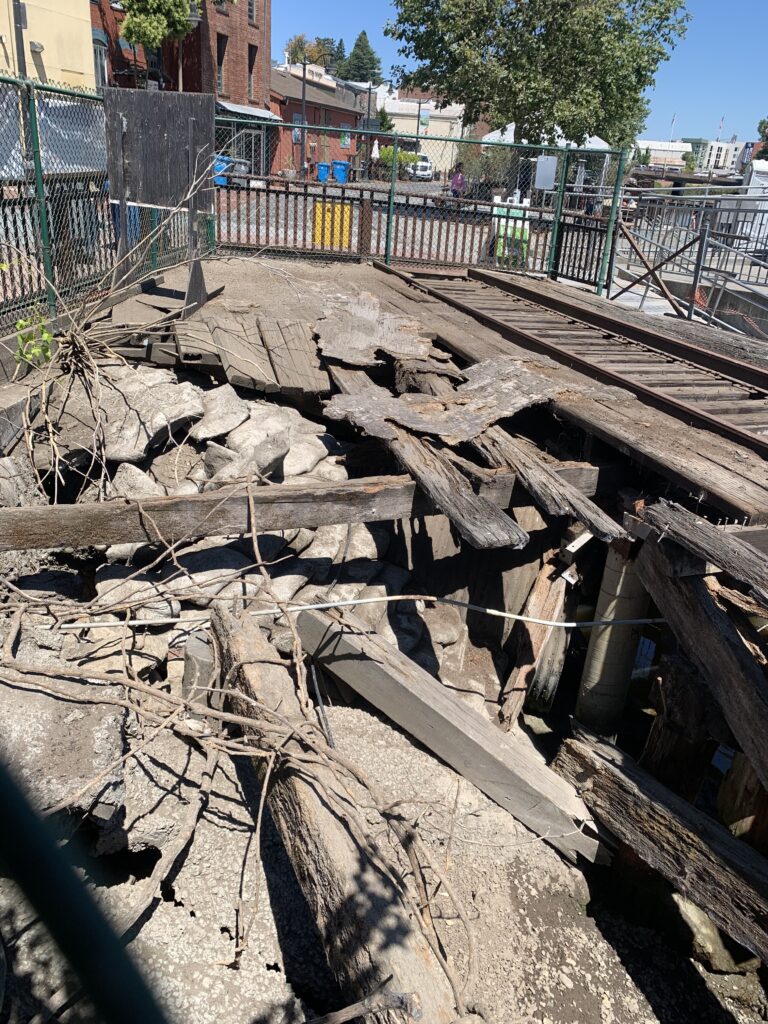 Deteriorating trestle surface. Train tracks to the right of the caved in decking.