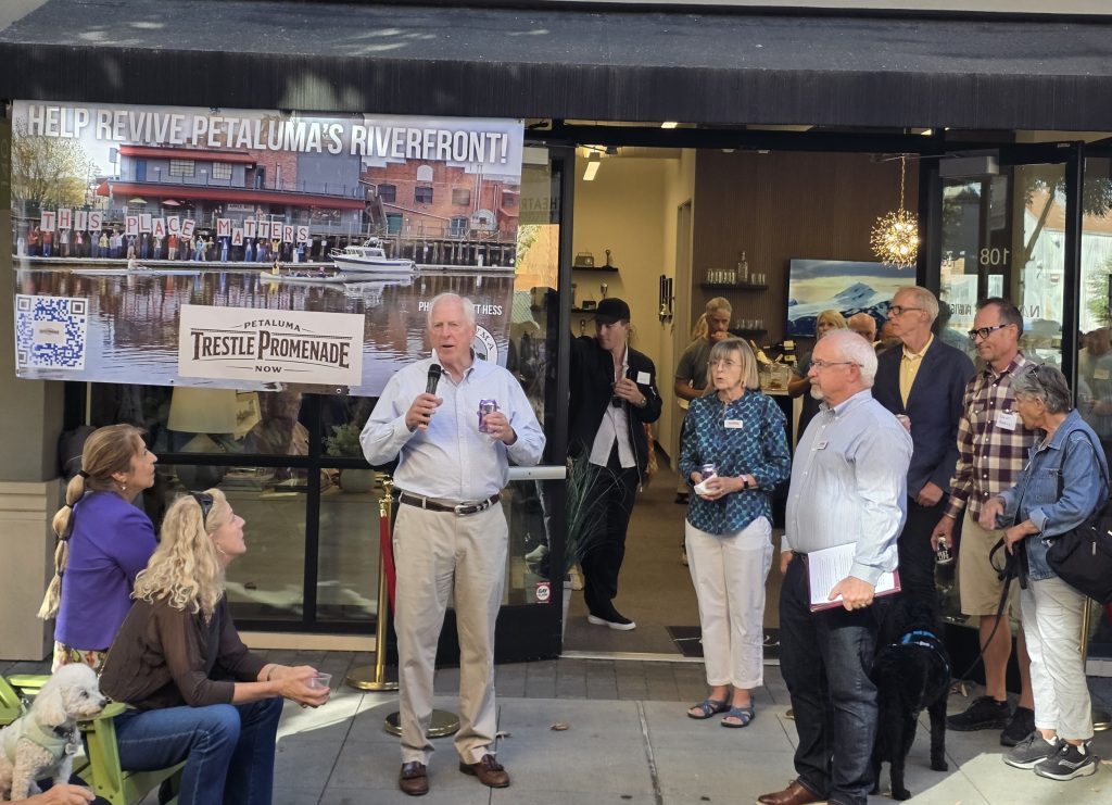 Party for the Promenade picture in front of Navigate RE in Theater Square. Congressman Mike Thompson is speaking into a microphone. Mayor Kevin McDonnell is next to him waiting to speak.
